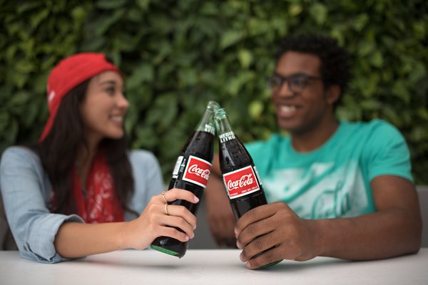 Two young adults enjoying bottles of Coke together.
