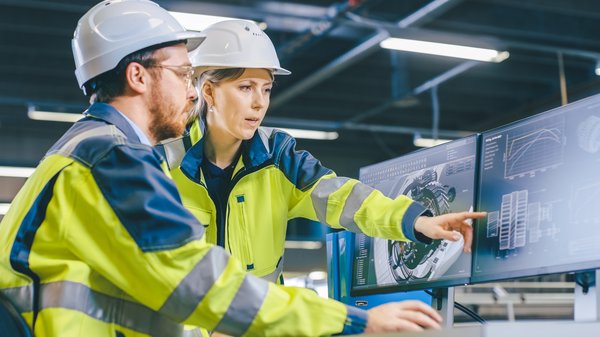 One construction worker points at blueprints on a computer screen while a colleague looks on.